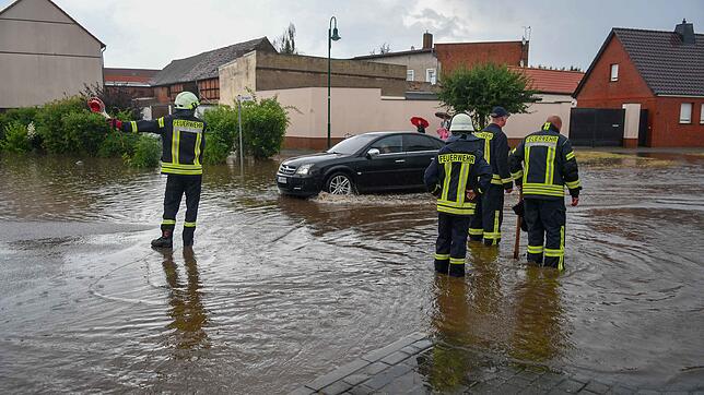 Feuerwehrmänner stehen nach Starkregen auf einer überfluteten Straße im Landkreis Börde, Sachsen-Anhalt.