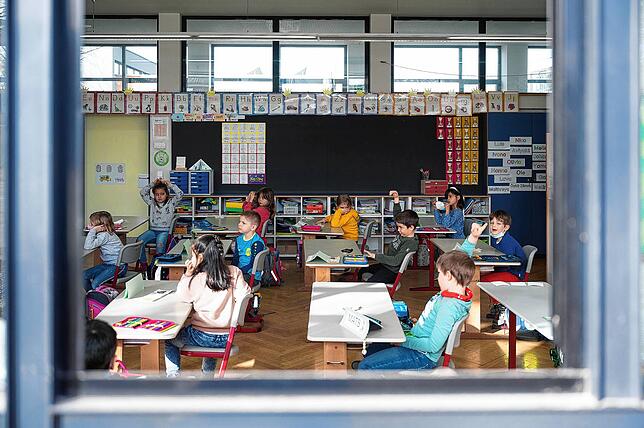 Kinder sitzen in einer ersten Klasse an einer Grundschule mit Wechselunterricht hinter einem offenen Fenster. Wie es nach den ...