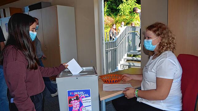 Die Achtklässlerin Maria (links) steckt ihren Wahlzettel in die Urne. Wahlhelferin Lotta kontrolliert die ordnungsgemäße Abgabe.