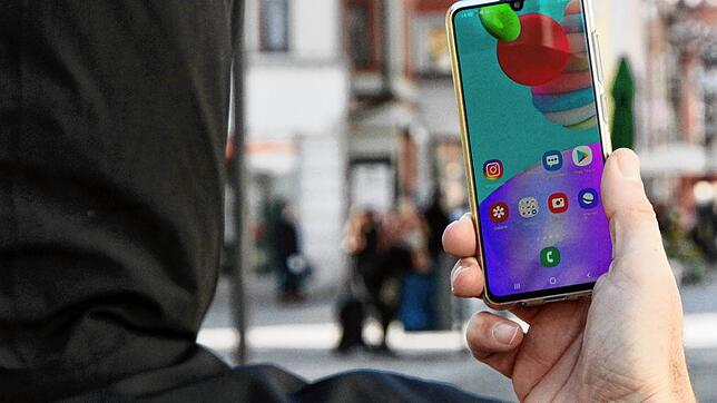 Ein Mann mit Kapuzenpulli schaut auf sein Handy. (Symbolbild)