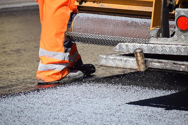 Hier ist der Absatz zu sehen. Der Arbeiter läuft etwas tiefer als die neue Asphalt-Deckschicht. Diese hat eine Höhe von vier Zentimetern.