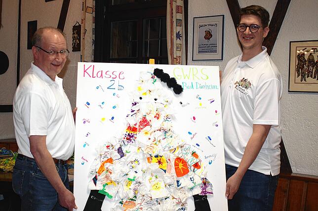 Ein mit Papiertaschentücher gestaltetes Kunstprojekt eines Salzhansels der Klasse 2b präsentieren Zunftmeister Volker Martin (links) und ...