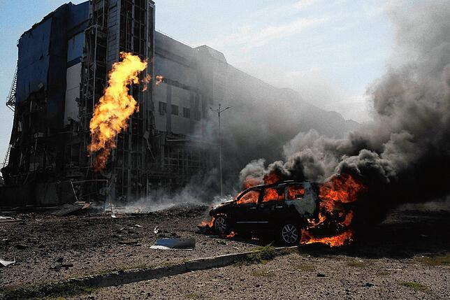 Nach russischen Bombenanschlägen brennt ein Auto vor einem durch die Angriffe beschädigten Geschäftszentrum in Charkiw in der Ukraine. ...