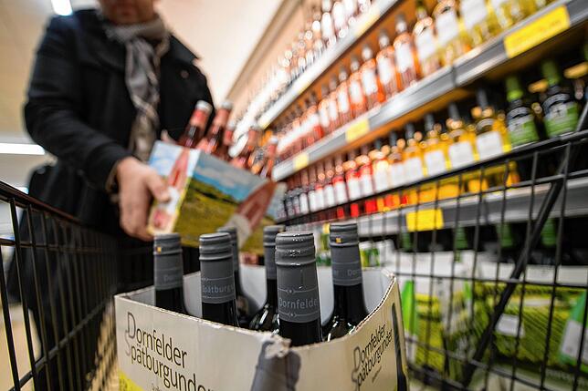 Ein Mann lädt in einer Filiale eines Discounters einen Karton mit Weinflaschen aus einem Weinregal in einen Einkaufswagen. ...