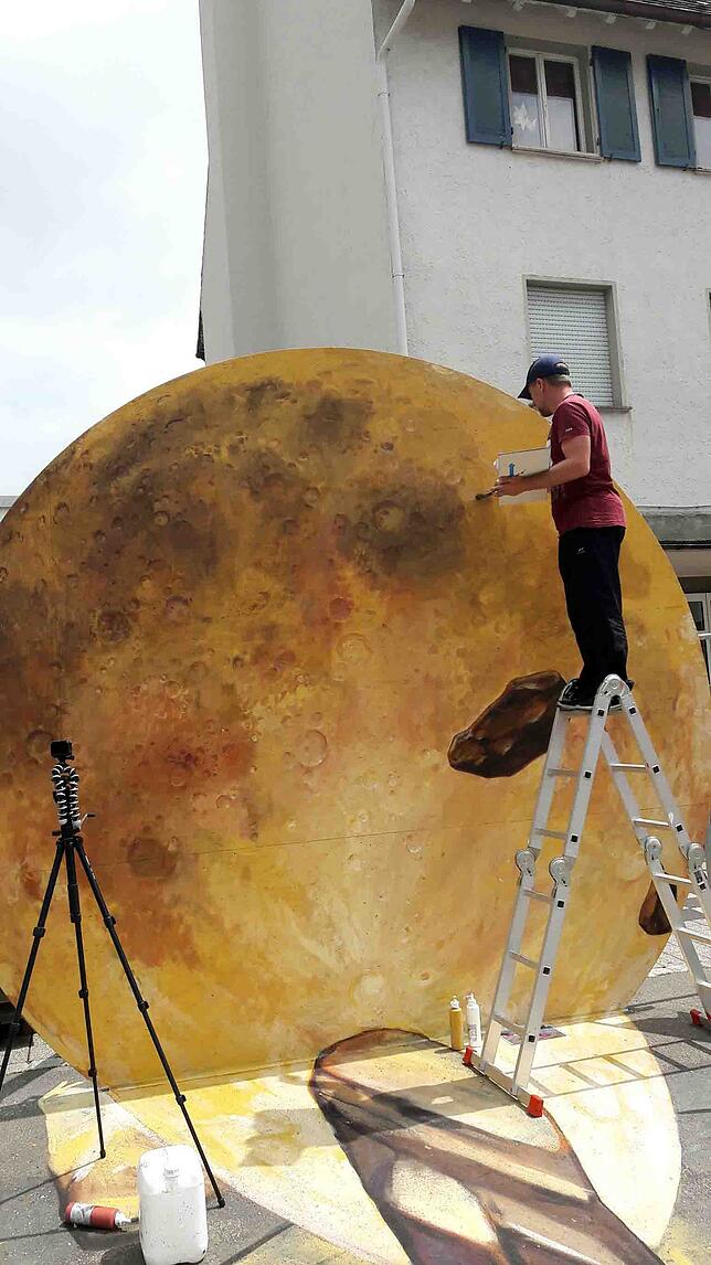 Auf der Leiter malt Nikolaj Arndt an der Sonne für sein großes 3D-Bild auf dem Blumberger Marktplatz. Bild: Bernhard Lutz