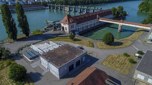 Das Bild zeigt das Energiedienst-Wasserkraftwerk Wyhlen. Neben dem langgestreckten Kraftwerksgebäude, das die Turbinen beherbergt, steht ...