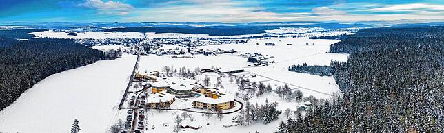 Luft-Aufnahme von der winterlichen Landschaft rund um die Nachsorgeklinik in Tannheim. Mittig im Hintergrund ist das Waldstück zu sehen, ...