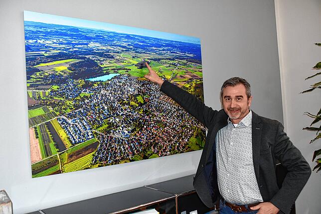 Hauptamtsleiter Roland Schmeh vor einem Luftbild von Steißlingen mit dem See, der bei Campern und Badegästen besonders beliebt ist.