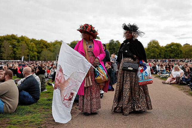 Zwei Frauen stehen mit einer Queen-Flagge im Hyde Park, während die Menschen das Staatsbegräbnis auf Großbildschirmen verfolgen.