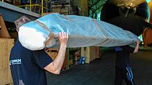 Eine Lieferung Längsträger: Das Bauteil, das die beiden Mitarbeiter hier geschultert haben, wird im Zeppelinhangar sicher deponiert und ...