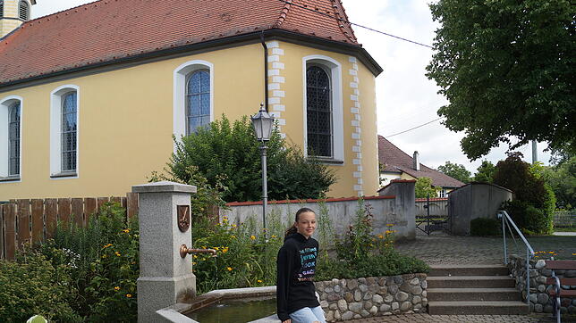 Leonie Werner steht hier am Dorfbrunnen bei der Kirche in der kleinen Seegemeinde Stetten.