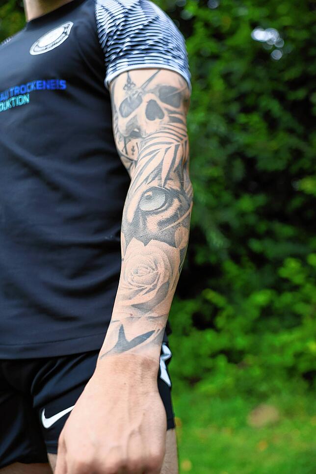 Auf Stockers linkem Arm sind eine Rose, ein Tiger und ein Totenkopf mit Uhr zu sehen.