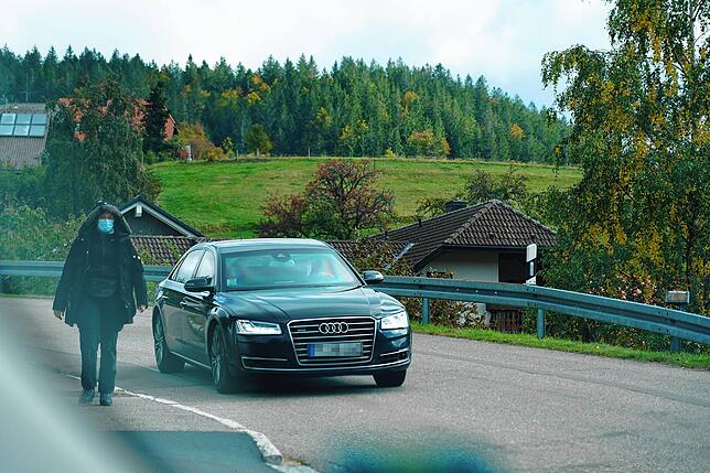 Eine Personenschützerin geht neben einem Fahrzeug, in dem mehrere Männer mit Mund-Nasen-Schutz sitzen. Die Scheiben der Limousine sind ...