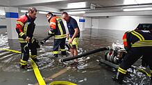 Knöcheltief stehen die Feuerwehrmänner im Wasser und montieren die Rohre einer Pumpe. Das Bild entstand im Untergeschoss im Parkhaus Post.