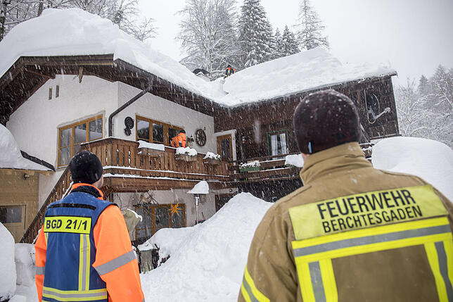 Feuerwehrmänner schaufeln am Mittwoch, 9. Januar, Schnee vom Dach eines Hauses in Berchtesgaden.