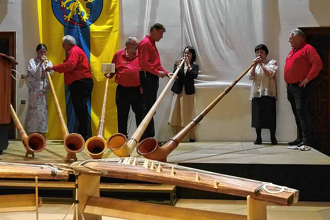 Die Alphorngruppe Meßkirch hilft nach ihrem Auftritt den japanischen Gästen, Töne mit dem Alphorn zu produzieren.