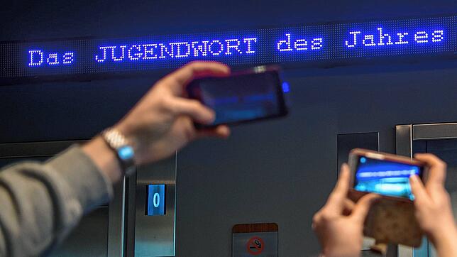 Auf einem Laufband erscheint „Jugendwort des Jahres“ über den digitalen Newsticker eines Hotels in München.