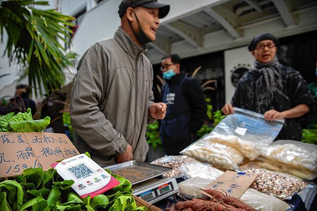 Ein Verkäufer auf einem Bauernmarkt in Peking spricht mit seinen Kunden: Das Schild neben der Wage hält einen QR-Code für die Zahlung ...