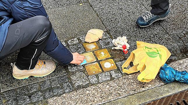 Die Stolpersteine in der Münsterstraße von der Familie Levi werden von Teilnehmern des Rundgangs geputzt.