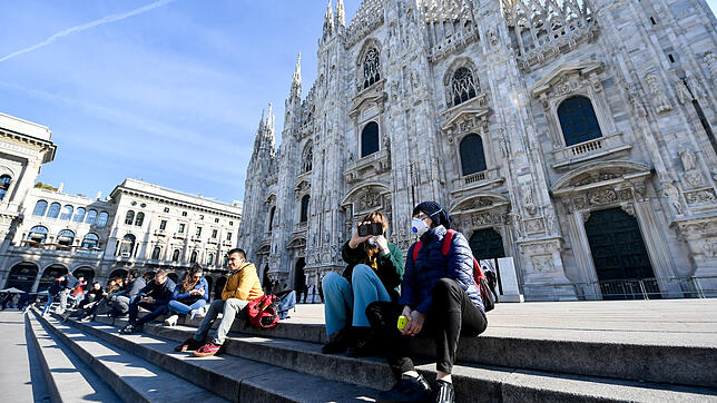 Touristen sitzen mit Schutzmasken auf den Stufen der Kathedrale von Mailand.