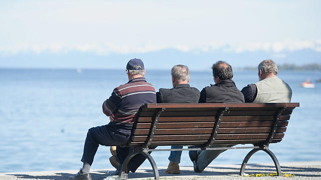 Vier Männer sitzen in Konstanz auf einer Bank am Ufer und blicken auf den Bodensee hinaus. Bild: dpa