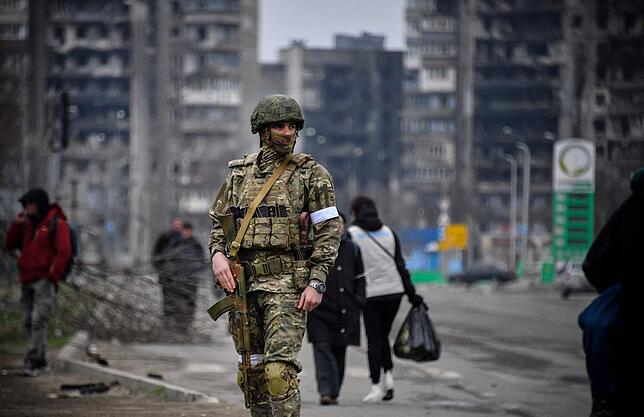 Ein russischer Soldat in der ukrainischen Stadt Mariupol, hinter ihm gehen Zivilisten entlang.