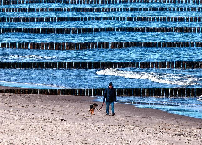 Ein Mann geht mit seinem Hund am ansonsten fast menschenleeren Ostseestrand in der Nähe der Seebrücke auf der Ostseeinsel Usedom ...