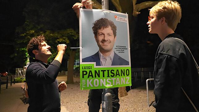 Kandidat Luigi Pantisano (links) hängt mit Hannah Gerster und Sebastian Lederer (hinter dem Plakat) Plakate für den OB-Wahkampf auf.