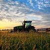 Ein Traktor steht vor der aufgehenden Sonne auf einem Feld.