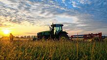 Ein Traktor steht vor der aufgehenden Sonne auf einem Feld.