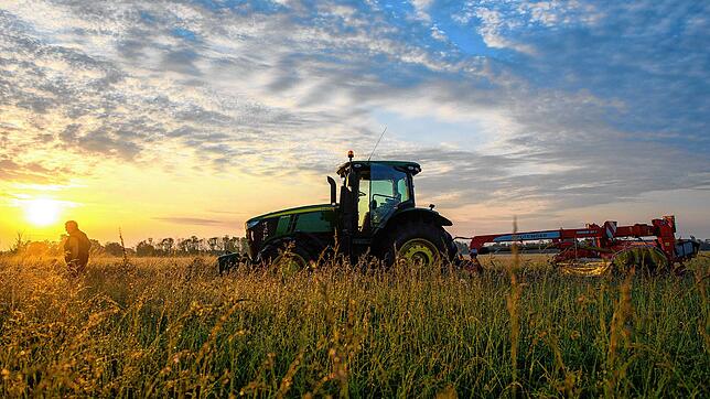 Ein Traktor steht vor der aufgehenden Sonne auf einem Feld.