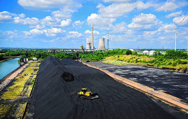 Steinkohle lagert im Hafen neben dem Kohlekraftwerk Mehrum und Windrädern im Landkreis Peine, Niedersachsen.