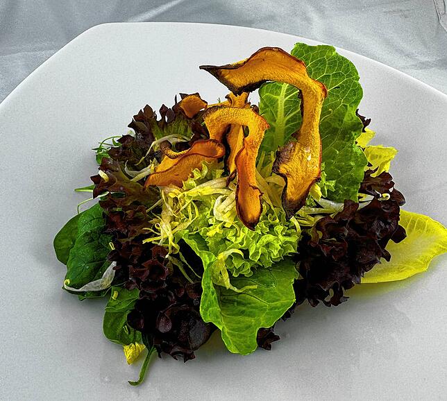 Vegane Vorspeise: Wildkräutersalat an einer Vinaigrette mit Kürbis-Chips.