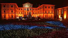 Das Barockschloss wird in wechselndes Licht getaucht. Davor flimmert das Lichtermeer.