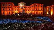 Das Barockschloss wird in wechselndes Licht getaucht. Davor flimmert das Lichtermeer.