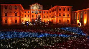 Das Barockschloss wird in wechselndes Licht getaucht. Davor flimmert das Lichtermeer.