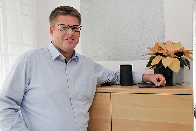 Jörg Putschbach steht in seinem Wohnzimmer neben einem der vier Echo-Sprachassistenten im Haus.
