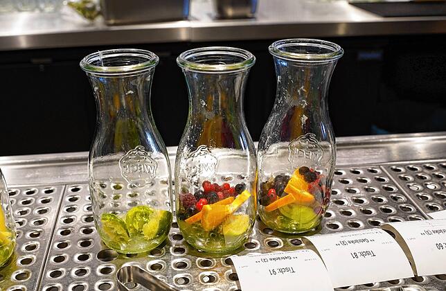 Vorbereitung der Pink-Berry-Limonade mit zerstoßenen Limetten, Orangenscheiben und bunten Beeren im Yoake.