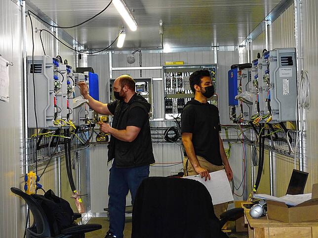 Damien aus Australien und Bilal aus Bahrein (von links) sind gerade dabei, einen weiteren Seecontainer mit der notwendigen Technik ...