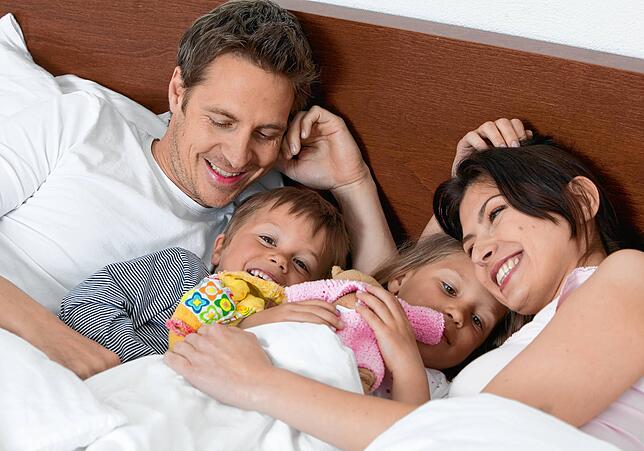 Eltern liegen mit Kindern im Bett: Dann kommt der Spaß im Liebesleben oft zu kurz.