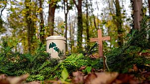 Eine Urne und ein Holzkreuz stehen in einem Friedwald (Symbolbild). Für immer mehr Menschen ist der Wald der beste Platz für die letzte ...