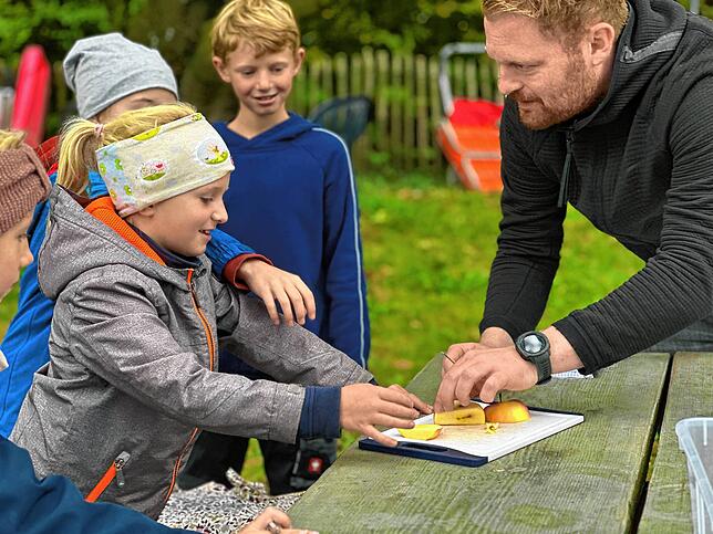 Apfel schneiden? Phila lässt lieber ihren Lehrer Lukas Wachter ran ans Messer. Ole schaut amüsiert zu.