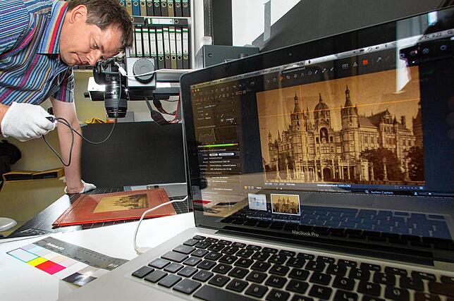 Ein wissenschaftlicher Mitarbeiter eines Museums nimmt eine historische Fotografie des Schweriner Schlosses auf. Durch die ...