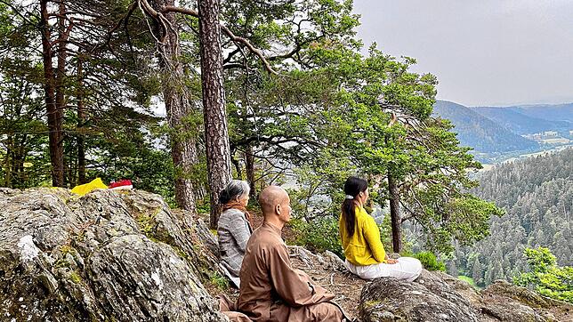 Vor der Gehmeditation lassen sich Mönch Thich Dao Chanh (Mitte) und Yogalehrerin Binh Le Thi (rechts) sitzend auf den Ort ein. Bild: ...