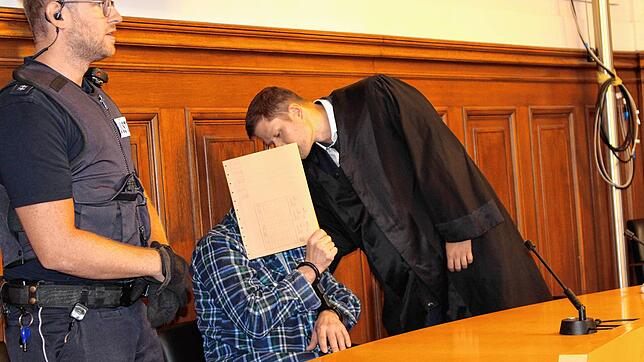 Der Angeklagte verbirgt sein Gesicht hinter einem Aktendeckel, während er mit seinem Verteidiger Benjamin Waldmüller spricht.