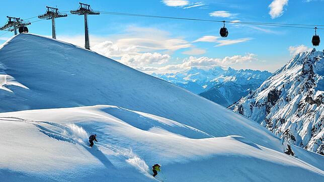 Freerider fahren unterhalb eines Skilifts am Arlberg hinab.