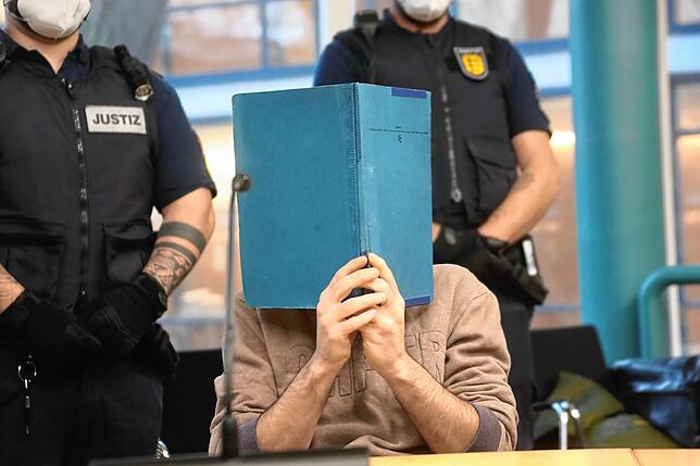 Der Angeklagte verbirgt sein Gesicht hinter Aktendeckeln.