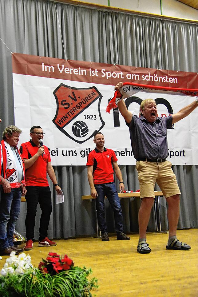 Vereinsmitglied Emil Bösch jubelt, als er seine Danksagung bekommt, und hält seinen SV Winterspüren – Schal in die Luft. Links ...