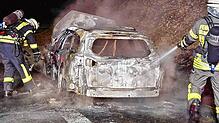 Einsatzkräfte der Feuerwehr löschen das ausgebrannte Fahrzeug.