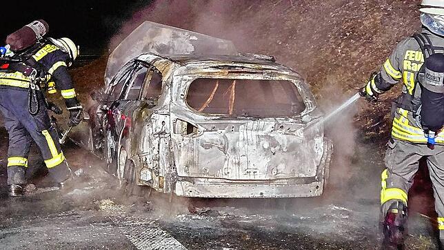 Einsatzkräfte der Feuerwehr löschen das ausgebrannte Fahrzeug.
